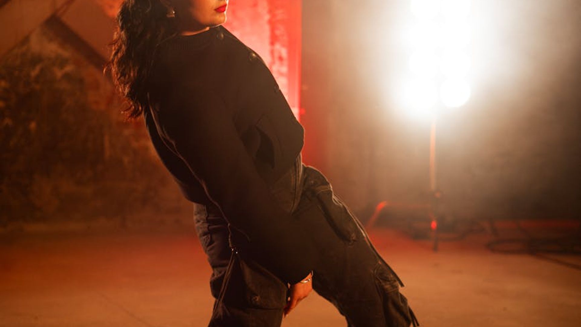 Person performing energetic movements in a dark studio setting.